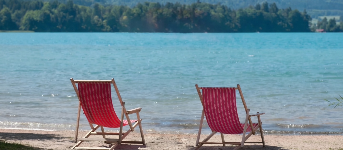 Zwei rote Liegestühle stehen am privaten Sandstrand des Weberhofs direkt am türkisblauen Faaker See in Egg, Kärnten